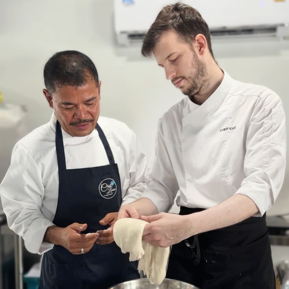 In the classroom, Chef Lucas provides hands-on assistance to students as they fold sourdough bread.