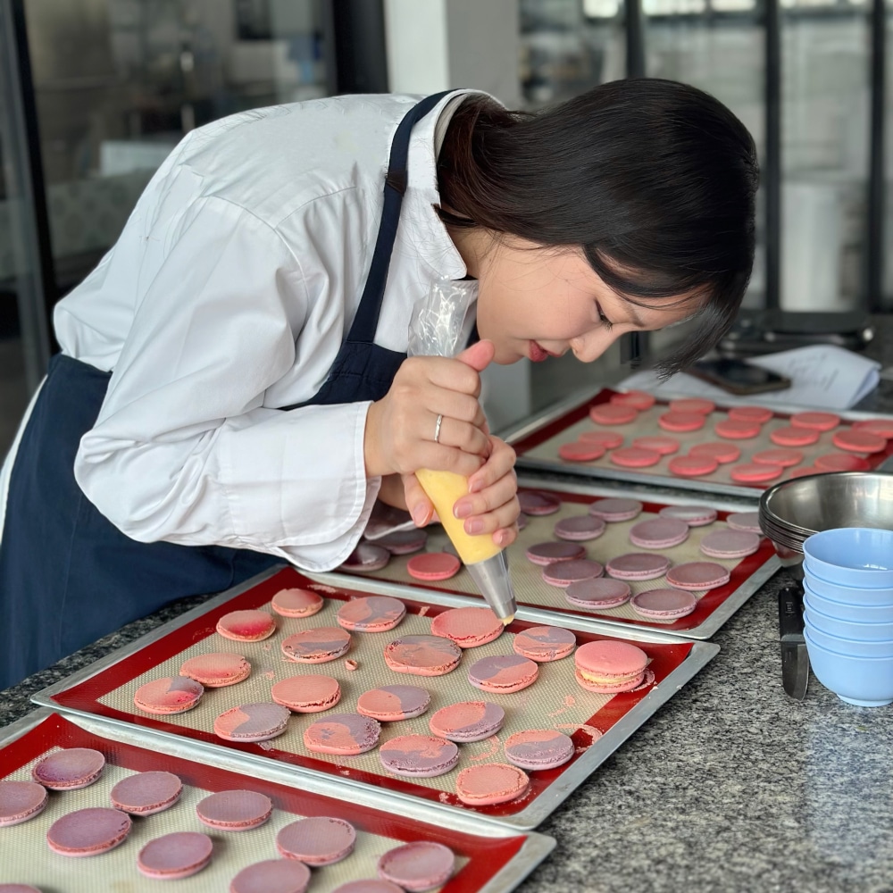 In the classroom, a student practices piping macaron filling with precision.